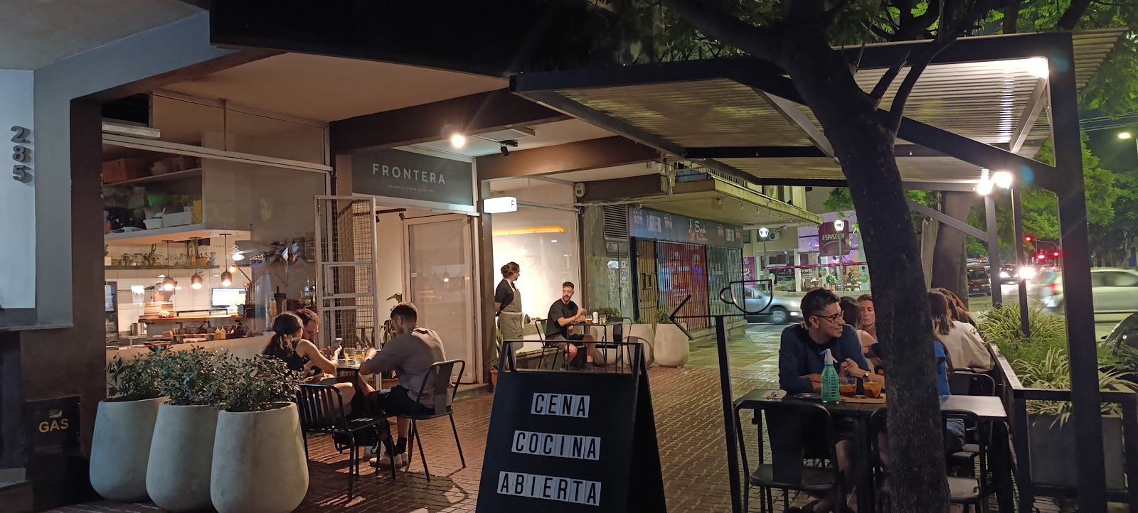 Frente nocturno de Frontera en Av. Pueyrredón, con mesas en la vereda y la cocina abierta a la vista.